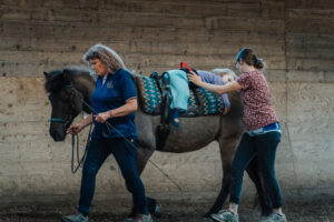 Ein behindertes Mädchen reitet auf einem Pferd als Teil der Hippotherapie-K bei Coaching Zeitgeschenk.
