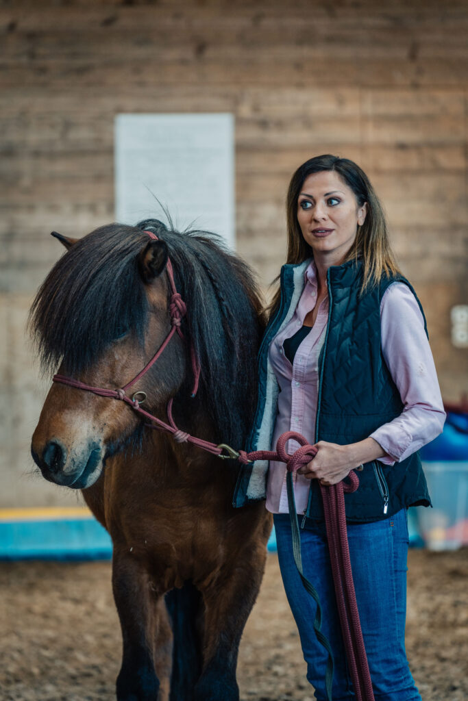 Eine Frau, die die Zügel eines Pferdes hält, als Teil eines therapeutischen Reitprogramms bei Coaching Zeitgeschenk.