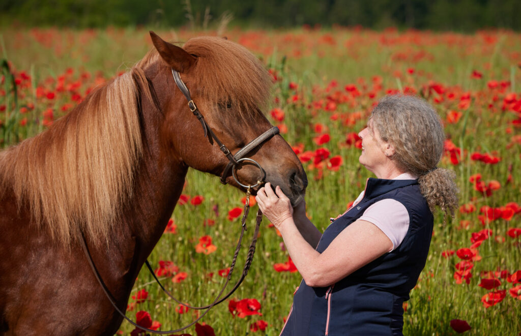 Karin Ettlins, die in einem Feld mit roten Mohnblumen auf ein Pferd schaut, während einer Einzelcoaching-Sitzung bei Coaching Zeitgeschenk.